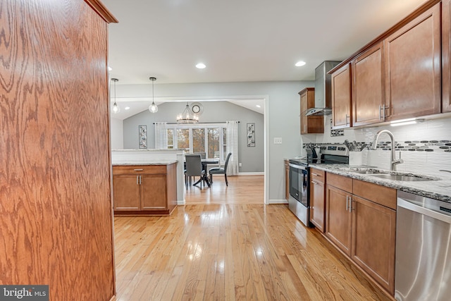 kitchen featuring wall chimney exhaust hood, sink, light stone counters, pendant lighting, and stainless steel appliances