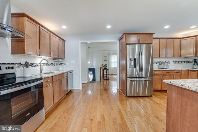 kitchen featuring sink, appliances with stainless steel finishes, range hood, light stone counters, and light wood-type flooring