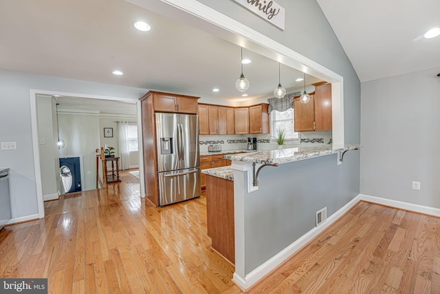 kitchen with a breakfast bar, stainless steel fridge with ice dispenser, light stone counters, kitchen peninsula, and light hardwood / wood-style flooring