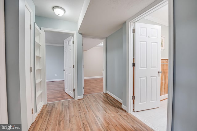 hall with crown molding, built in shelves, and light hardwood / wood-style floors