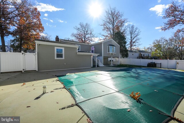 rear view of property featuring a covered pool and a patio