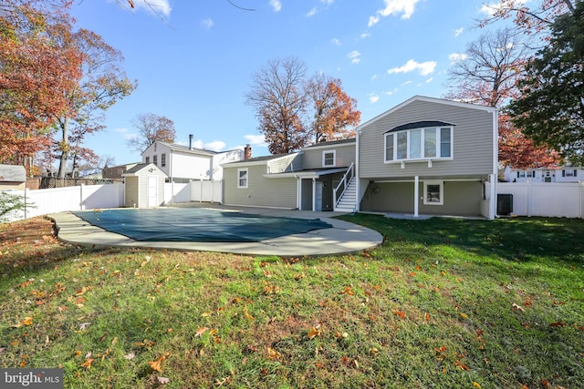 rear view of house with a patio area, central air condition unit, a covered pool, a yard, and a storage unit