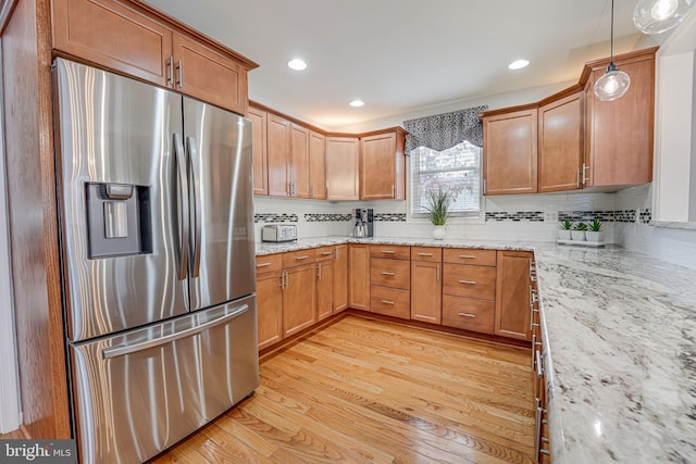 kitchen featuring decorative backsplash, hanging light fixtures, stainless steel fridge with ice dispenser, light stone countertops, and light hardwood / wood-style flooring