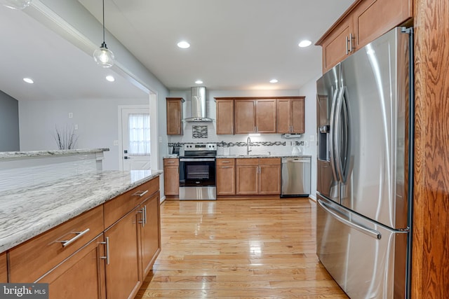 kitchen featuring appliances with stainless steel finishes, decorative light fixtures, tasteful backsplash, sink, and wall chimney range hood