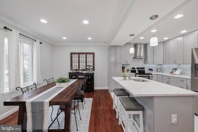 kitchen with sink, gray cabinetry, an island with sink, light stone countertops, and wall chimney range hood