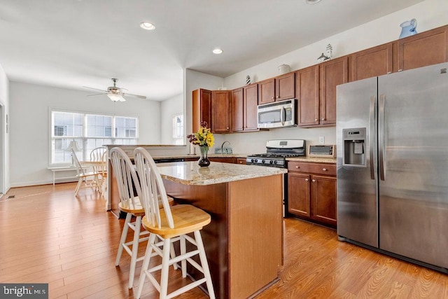 kitchen featuring a kitchen breakfast bar, a center island, ceiling fan, light hardwood / wood-style floors, and stainless steel appliances