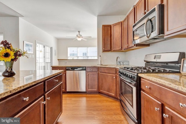 kitchen with sink, ceiling fan, light stone counters, stainless steel appliances, and light hardwood / wood-style floors