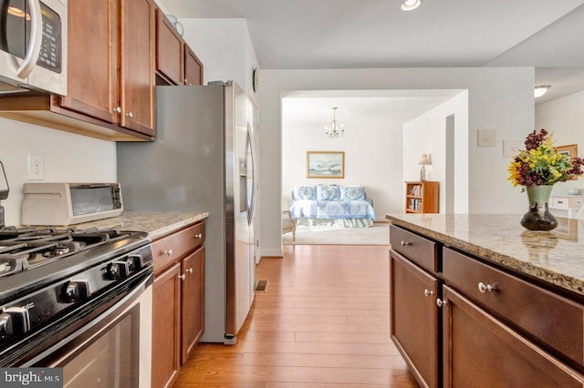 kitchen featuring light stone counters, decorative light fixtures, appliances with stainless steel finishes, a notable chandelier, and light hardwood / wood-style floors