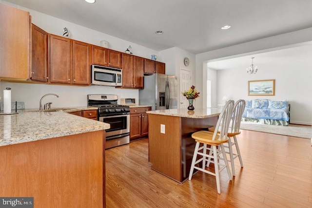 kitchen featuring sink, a breakfast bar, appliances with stainless steel finishes, light stone counters, and a kitchen island