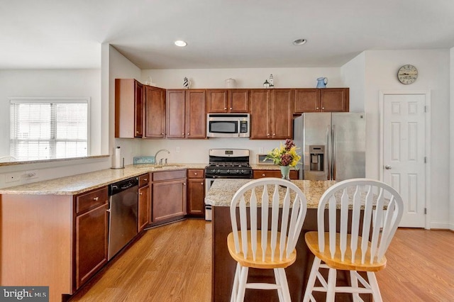 kitchen featuring light stone counters, light hardwood / wood-style floors, stainless steel appliances, and a breakfast bar