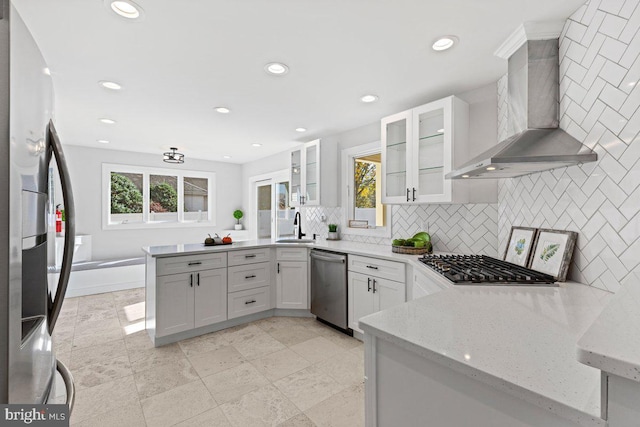 kitchen featuring sink, white cabinetry, stainless steel appliances, light stone countertops, and wall chimney range hood