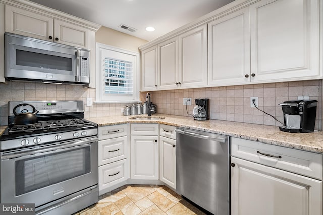 kitchen featuring appliances with stainless steel finishes, sink, white cabinets, decorative backsplash, and light stone counters