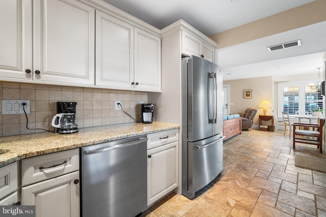 kitchen with tasteful backsplash, appliances with stainless steel finishes, white cabinets, and light stone counters