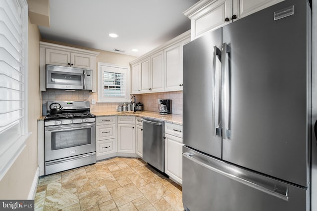 kitchen featuring appliances with stainless steel finishes, light stone counters, white cabinets, and backsplash