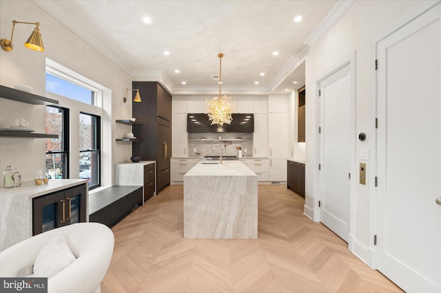 kitchen featuring decorative light fixtures, sink, white cabinets, light parquet floors, and a center island with sink