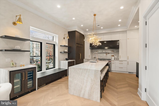 kitchen featuring white cabinetry, decorative light fixtures, a center island with sink, and light parquet floors