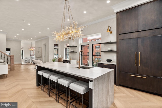 kitchen with sink, a breakfast bar area, light parquet floors, paneled built in refrigerator, and a center island with sink