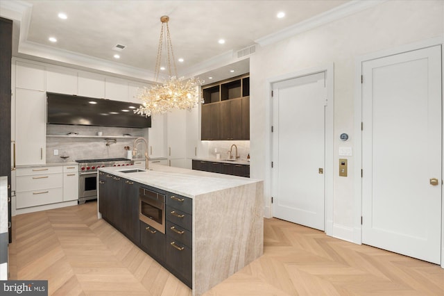 kitchen with appliances with stainless steel finishes, decorative light fixtures, white cabinets, a kitchen island with sink, and light parquet flooring