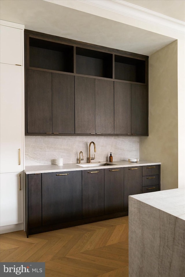 kitchen featuring sink, crown molding, dark brown cabinets, light parquet floors, and backsplash