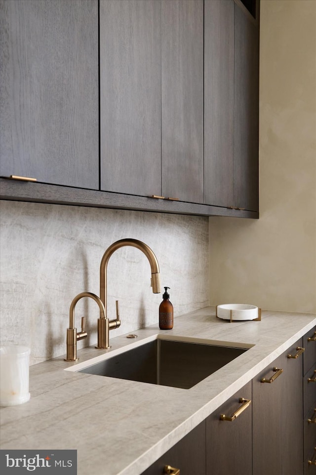 interior details featuring light stone counters, sink, decorative backsplash, and gray cabinetry