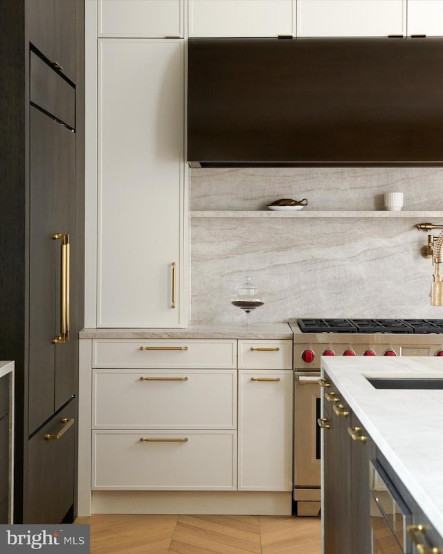 kitchen featuring white cabinetry, light stone countertops, high end stove, and range hood