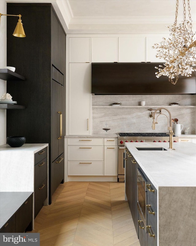 kitchen with pendant lighting, crown molding, range hood, white cabinets, and light parquet flooring