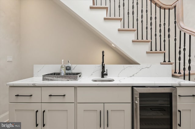 bar with light stone counters, beverage cooler, sink, and white cabinets