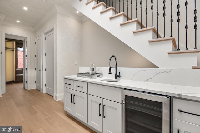 bar featuring sink, wine cooler, light stone counters, light hardwood / wood-style floors, and white cabinets