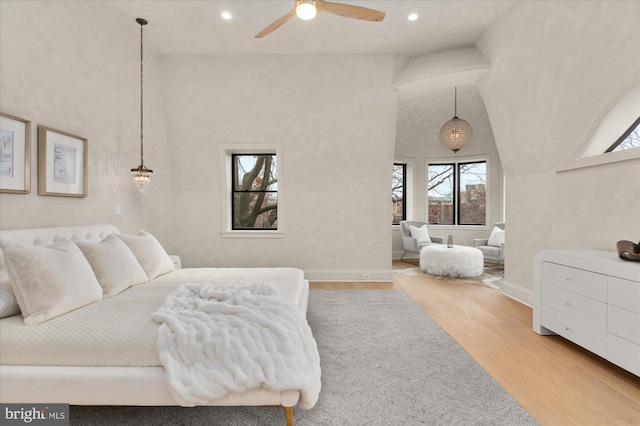 bedroom with light hardwood / wood-style floors, ceiling fan, and a high ceiling