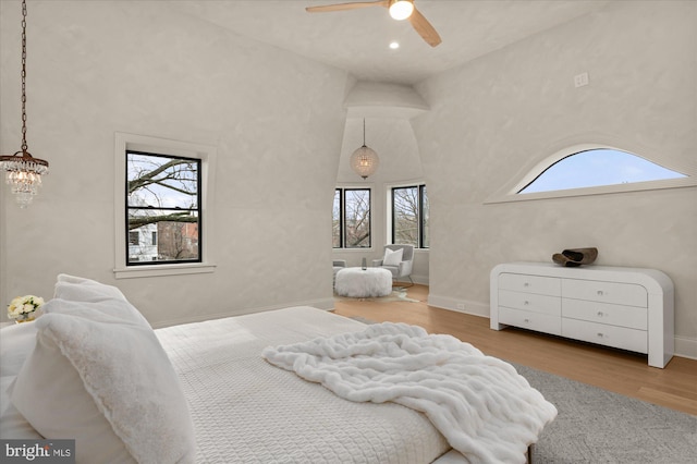 bedroom with multiple windows, ceiling fan with notable chandelier, high vaulted ceiling, and light hardwood / wood-style flooring