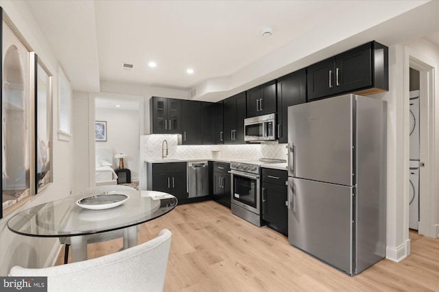 kitchen with stacked washer and dryer, sink, stainless steel appliances, light hardwood / wood-style floors, and backsplash