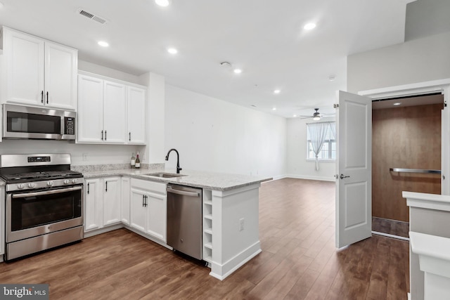 kitchen featuring sink, appliances with stainless steel finishes, light stone countertops, white cabinets, and kitchen peninsula