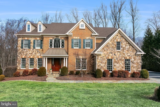 colonial-style house featuring a shingled roof, a front yard, stone siding, and brick siding