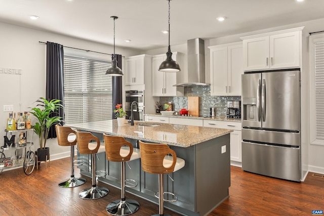 kitchen with white cabinetry, an island with sink, sink, stainless steel appliances, and wall chimney exhaust hood