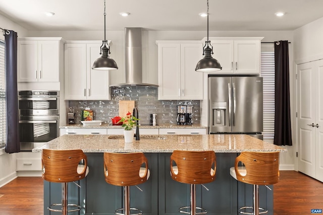 kitchen featuring white cabinetry, a kitchen island with sink, stainless steel appliances, and wall chimney exhaust hood