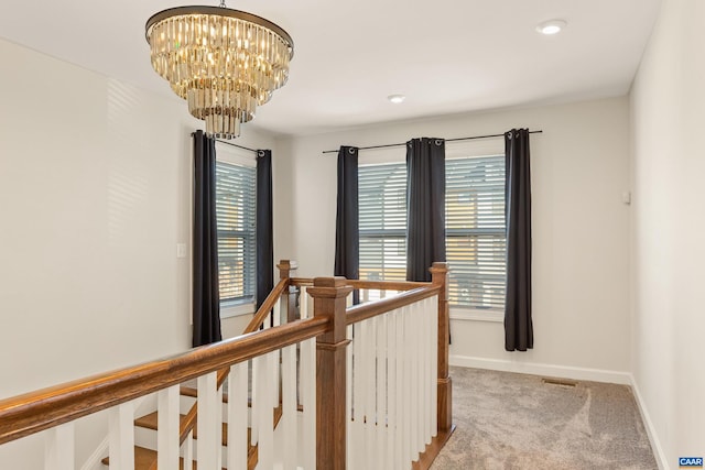 hallway featuring an inviting chandelier and light carpet