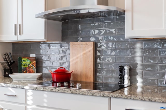 kitchen with stone counters, white cabinets, backsplash, and wall chimney exhaust hood