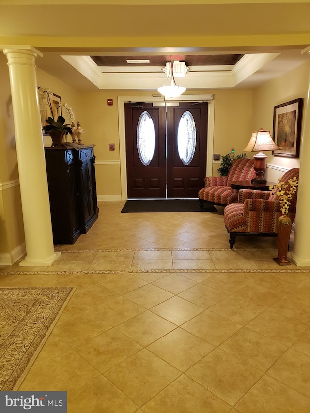 foyer with ornamental molding, a tray ceiling, light tile patterned floors, and decorative columns