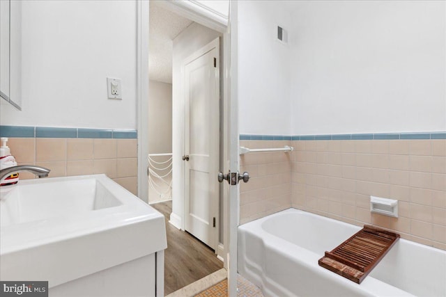 bathroom with vanity, a bath, tile walls, and a textured ceiling