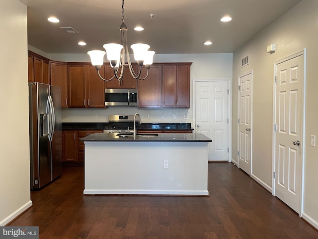 kitchen with a kitchen island with sink, pendant lighting, dark wood-type flooring, and appliances with stainless steel finishes