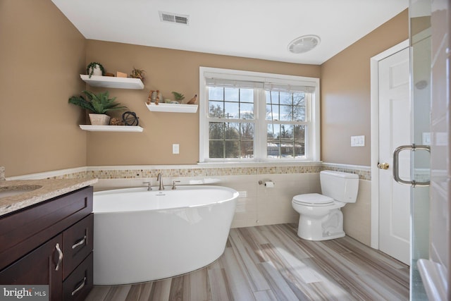 bathroom with tile walls, hardwood / wood-style floors, vanity, a tub to relax in, and toilet