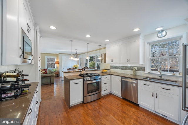 kitchen featuring pendant lighting, sink, stainless steel appliances, white cabinets, and kitchen peninsula