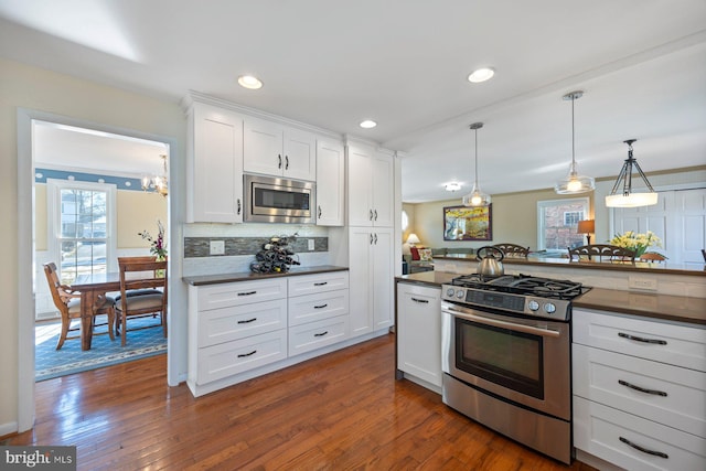 kitchen featuring hanging light fixtures, backsplash, stainless steel appliances, white cabinets, and dark hardwood / wood-style flooring