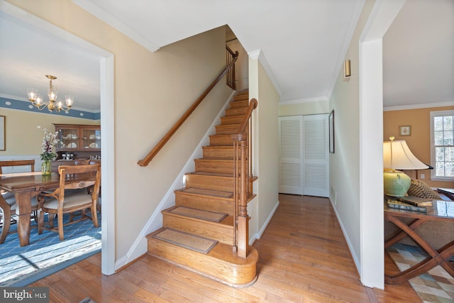 stairs with crown molding, hardwood / wood-style floors, and a notable chandelier