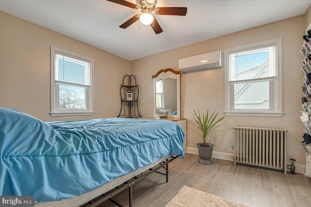 bedroom with radiator heating unit, light hardwood / wood-style floors, multiple windows, and an AC wall unit