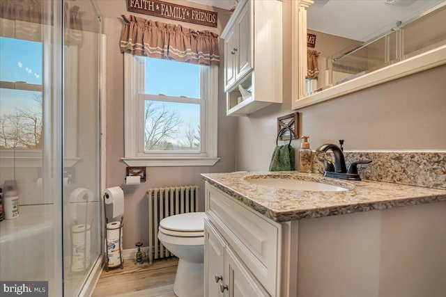 bathroom featuring radiator, hardwood / wood-style flooring, vanity, toilet, and walk in shower