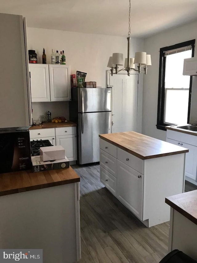 kitchen featuring butcher block counters, decorative light fixtures, a center island, stainless steel refrigerator, and white cabinets