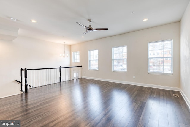 spare room featuring a healthy amount of sunlight, dark hardwood / wood-style floors, and ceiling fan with notable chandelier