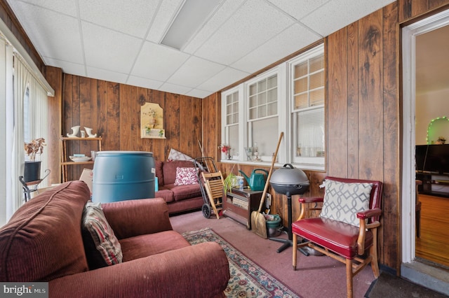 living room with a drop ceiling, wooden walls, and carpet