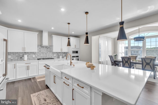 kitchen featuring sink, hanging light fixtures, white cabinets, built in microwave, and wall chimney exhaust hood